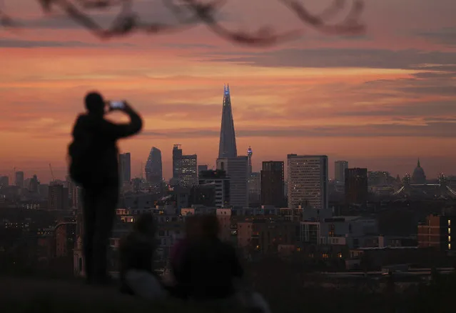 A person takes a photo of the skyline with the Shard building in the center, at sunset, from Greenwich Park in London, Tuesday, November 24, 2020. (Photo by Yui Mok/PA Wire via AP Photo)