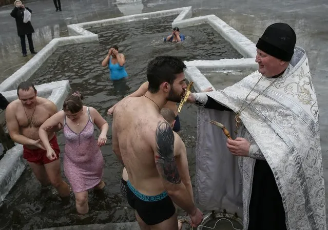 A priest takes part in a religious ceremony as people take a dip in a lake during Orthodox Epiphany celebrations in Kiev January 19, 2015. (Photo by Gleb Garanich/Reuters)