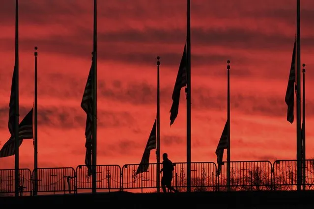 A solitary runner passes under the flags hanging at half-staff surrounding the Washington Monument at day break in Washington, Wednesday, February 24, 2021. President Joe Biden ordered the flags to be lowered in honor of the 500,000 lives lost to COVID-19 in the U.S. (Photo by J. David Ake/AP Photo)