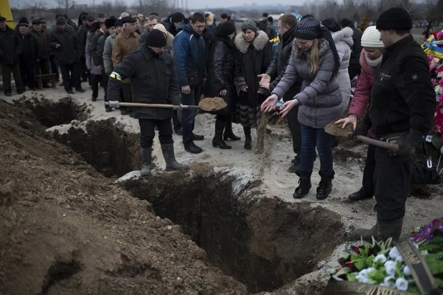 Relatives of Alexander Demyanenko, victim of Saturday shelling pour soil at his grave during funerals in Mariupol, Ukraine, on Monday January 26, 2015. (Photo by Evgeniy Maloletka/AP Photo)