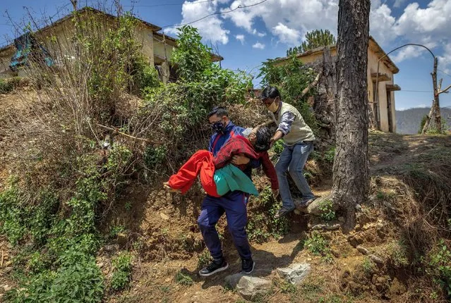 Pramila Devi, 36, who is suffering from the coronavirus disease (COVID-19), is carried by her nephew Rajesh Kumar, as he takes her to a local government dispensary in Kaljikhal, in the northern state of Uttarakhand, India, May 23, 2021. (Photo by Danish Siddiqui/Reuters)