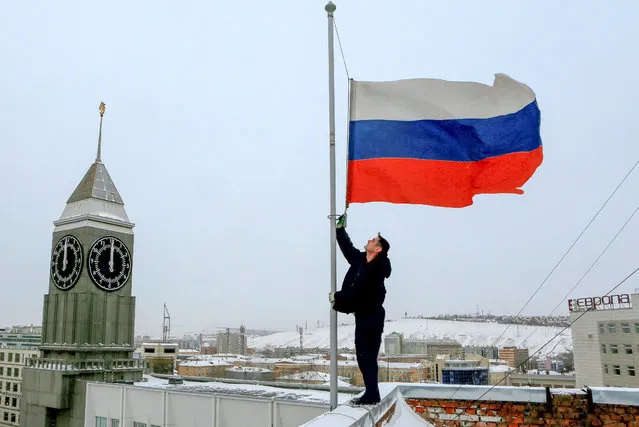 A worker lowers the Russian national flag to half-mast on a roof of the city administration building, as the country observes a day of mourning for victims of the Tu-154 plane which crashed into the Black Sea on its way to Syria on Sunday, in Krasnoyarsk, Russia, December 26, 2016. (Photo by Ilya Naymushin/Reuters)