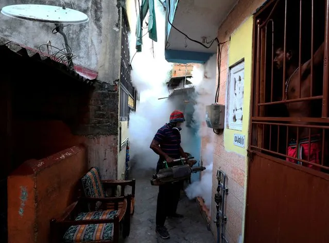 A resident watches as a health worker fumigates against mosquitoes in a residential area, as Sri Lanka tries to curb dengue fever across the island in Colombo, Sri Lanka on July 12, 2023. (Photo by Dinuka Liyanawatte/Reuters)
