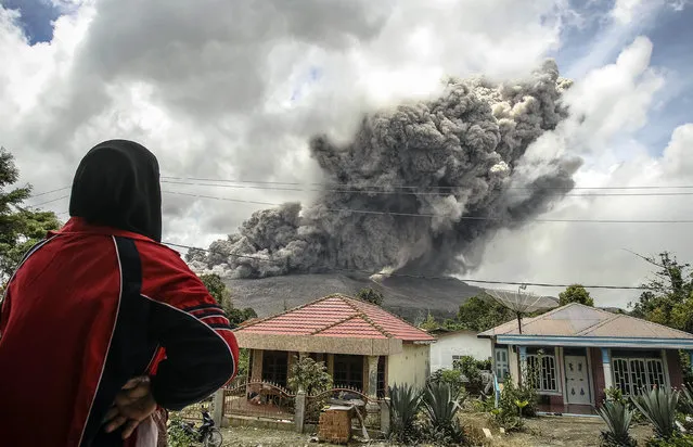 A woman in a village in Karo regency watches Mount Sinabung erupt in Indonesia's North Sumatra province, October 8, 2014. (Photo by Y. T. Haryono/Reuters)