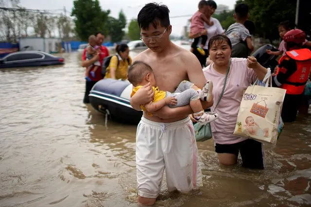 A man holding a baby wades through a flooded road following heavy rainfall in Zhengzhou, Henan province, China on July 22, 2021. (Photo by Aly Song/Reuters)