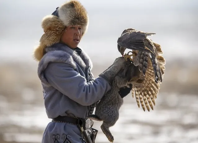 A hunter holds a rabbit caught by his tamed hawk during the traditional hunting contest outside the village of Nura, east from Almaty, Kazakhstan, February 13, 2016. (Photo by Shamil Zhumatov/Reuters)