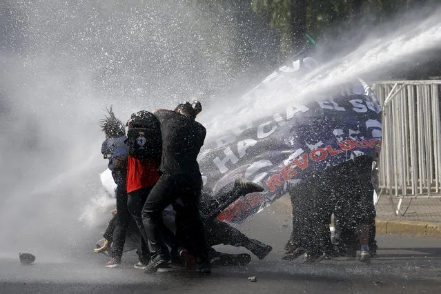 Protesters are hit by a jet of water released from a riot police vehicle during a demonstration against the government to demand changes in the education system at Santiago, April 16, 2015. (Photo by Ivan Alvarado/Reuters)