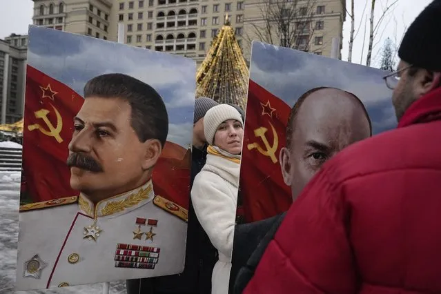 A Communist Party supporter stands between portraits of Soviet leaders Joseph Stalin, left, and Vladimir Lenin on Manezhnaya Square decorated for the New Year and Christmas festivities near the Kremlin Wall in Moscow, Russia, Thursday, December 21, 2023 marking the 144th anniversary of Stalin's birth. (Photo by Alexander Zemlianichenko/AP Photo)