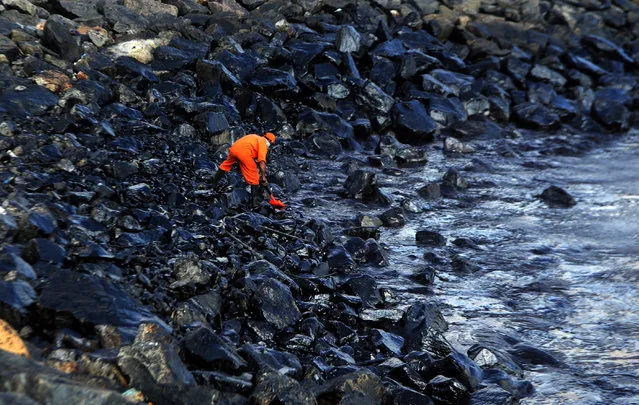 A member of the Pollution Response Team collects a sample of an oil spill from boulders at the coast, a day after an oil tanker and an LPG tanker collided off Kamarajar Port in Ennore, in Chennai on January 30, 2017. (Photo by Arun Sankar/AFP Photo)