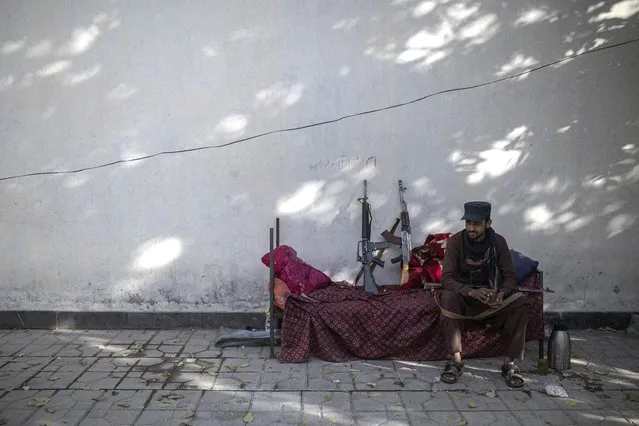 A Taliban fighter sits outside the government passport office, re-opened after Taliban announced they would be issuing a backlog of applications approved by the previous administration in Kabul, Afghanistan, Sunday, October 17, 2021. (Photo by Ahmad Halabisaz/AP Photo)