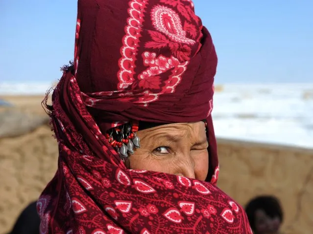 An Afghan internally displaced woman covers her face as she stands in Sakhi camp in Mazar-i-Sharif on February 10, 2014. Many families were forced to flee their homes in southern Afghanistan due to Taliban fighting and are forced to spend the harsh winter season at the camp in poverty. (Photo by Farshad Usyan/AFP Photo)