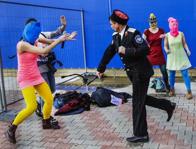 A Cossack militiaman attacks Nadezhda Tolokonnikova and a photographer as she and fellow members of the punk group p*ssy Riot, including Maria Alekhina, right, in the pink balaclava, stage a protest performance in Sochi, Russia, on February 19, 2014. (Photo by Morry Gash/Associated Press)