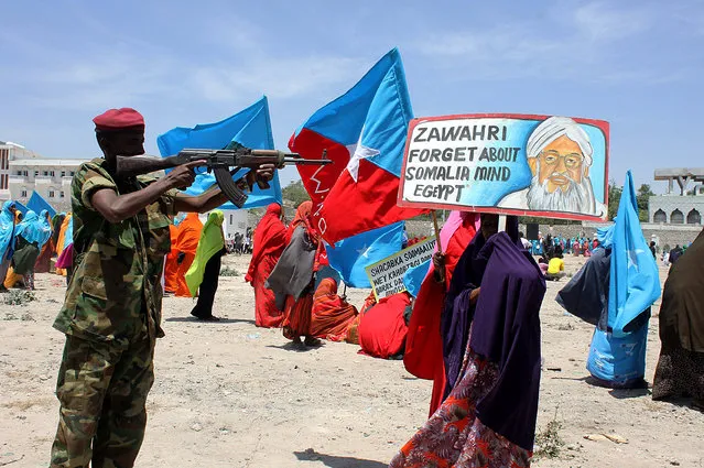 A Somali security soldier points his weapon at a poster bearing a photo of Al-Qaeda leader Ayman al-Zawahiri during an anti Al-shabab rally in Mogadishu on February 23, 2014. (Photo by Abdifitah Hashi/AFP Photo)