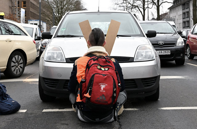 A car stands right in front of a climate change activist who is glued to a street and blocks the traffic during rush hour in Cologne, Germany on February 3, 2023. (Photo by Jana Rodenbusch/Reuters)