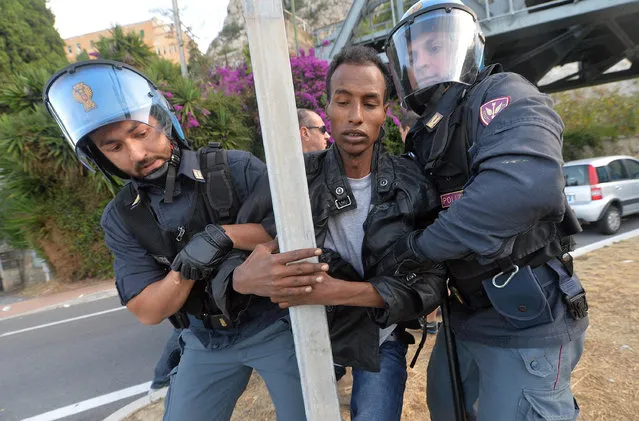 A migrant holds onto a signpost as Italian Police officers drag him away, in Ventimiglia, at the Italian-French border Tuesday, June 16, 2015. Police at Italy's Mediterranean border with France have forcibly removed some of the African migrants who have been camping out for days in hopes of continuing their journeys farther north. The migrants, mostly from Sudan and Eritrea, have been camped out for five days after French border police refused to let them cross. (Luca Zennaro/ANSA via AP)