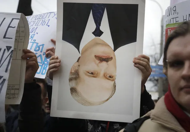 A protestor holds overturned portrait of Belorussian President Alexander Lukashenko during a rally in Minsk, Belarus, Wednesday, March 15, 2017. Wednesday's march in the capital Minsk and smaller rallies at several other Belarusian cities were the latest in a series of demonstrations against the law that obliges citizens to pay the equivalent of $250 if they work less than half the year and do not register with state labor exchanges. (Photo by Sergei Grits/AP Photo)