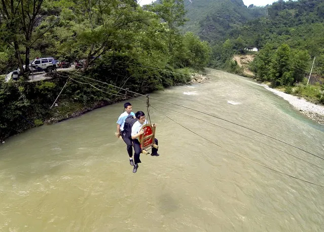 Court officers hold a national emblem as they ride a zip-line across a river, to attend a mobile court hearing of a divorce dispute, in Huilong village of Fengjie county, Chongqing municipality, China, June 9, 2015. (Photo by Reuters/Stringer)