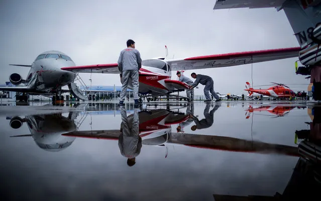 Three men push a Skywave light sport aircraft on the tarmac before the start of the 2017 Asian Business Aviation Conference and Exhibition (ABACE) at Shanghai's Hongqiao Airport on April 10, 2017. ABACE will be held at Shanghai Hongqiao Airport from April 11 to 13. (Photo by Johannes Eisele/AFP Photo)