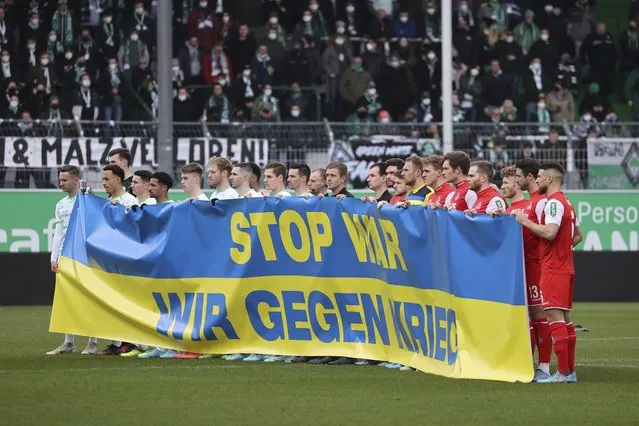 At the start of the match, the players of both teams hold a Ukrainian flag with the inscription “Stop War. We against war” prior the Bundesliga soccer match between Greuther Fuerth and 1. FC Cologne in Fuerth, Germany, Saturday, February 26, 2022. (Photo by Daniel Karmann/dpa via AP Photo)