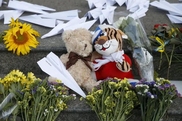 Flowers, toys and self-made paper planes are left to commemorate the victims of the Malaysia Airlines flight MH17 plane crash a year ago outside the Dutch embassy in Kiev, Ukraine, July 17, 2015. (Photo by Valentyn Ogirenko/Reuters)