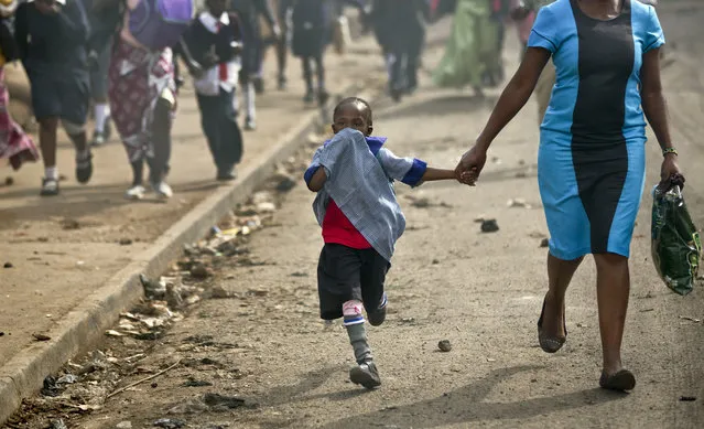 A young schoolgirl overcome by tear gas runs to safety, as police firing tear gas engage protesters throwing rocks in the Kibera slum of Nairobi, Kenya Monday, May 23, 2016. (Photo by Ben Curtis/AP Photo)