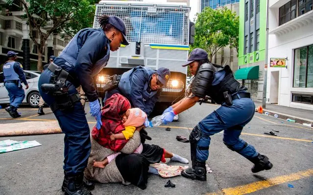 A woman holds onto her baby as South African Police officers forcefully remove refugees from various countries who were camping outside the Cape Town offices of the United Nations Council for refugees, In Cape Town on October 30, 2019. Violent scuffles break out in Cape Town as riot police remove refugees outside the UN high Commission for Refugees (UNHCR) office. Protesters were holding a sit-in for 24 days over the safety of foreign nationals in the city. (Photo by AFP Photo/Stringer)