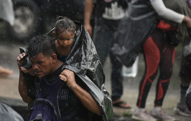 A migrant heading in a caravan to the US, carries a toddler under the rain as he walks towards Mexico City to request asylum and refugee status in Huixtla, Chiapas State, Mexico, on October 25, 2021. (Photo by Isaac Guzman/AFP Photo)