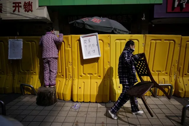 A resident pays for groceries by standing on a tree stump to peer over barriers set up to ring fence a wet market on a street in Wuhan, Hubei province, China, April 1, 2020. Life in the Chinese city of Wuhan, where the coronavirus first emerged, is slowly returning to normal as the government relaxes a more than two-month-old lockdown that cut the city off from the world and kept most of its 11 million residents at home. (Photo by Aly Song/Reuters)