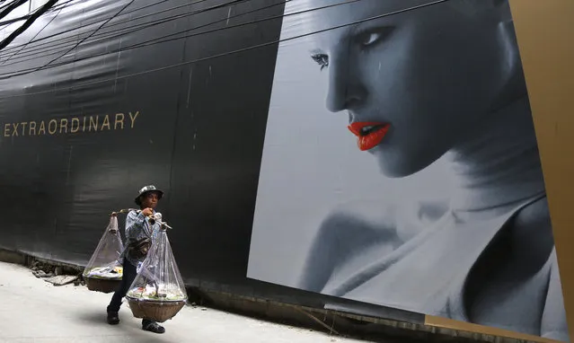 A Thai street food-seller walks the streets passing a high-end, luxury shopping center construction site boarded with advertisements of fashion models, in Bangkok, Thailand, August 21, 2014. (Photo by Barbara Walton/EPA)