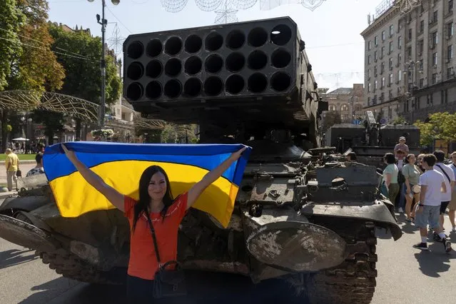 A woman poses for a picture with a national flag as she visits an exhibition of destroyed Russian military vehicles and weapons, dedicated to the upcoming country's Independence Day, amid Russia's attack on Ukraine, in the centre of Kyiv, Ukraine on August 21, 2022. (Photo by Valentyn Ogirenko/Reuters)