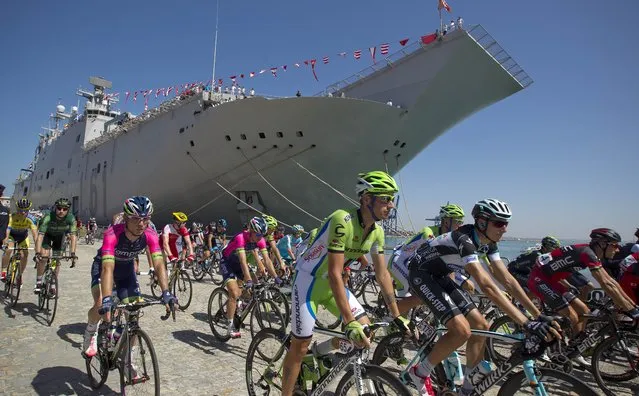 Riders past the Príncipe de Asturias aircraft carrier, the only one in the Spanish navy's possession, at the start of the third stage of the Vuelta, tour of Spain cycle race, in Cadiz, Spain, on Monday August 25, 2014. The third stage of the Spanish Vuelta cycling race over 188 kilometers with start in Cadiz and finish in Arcos de La Frontera. (Photo by Miguel Angel Morenatti/AP Photo)