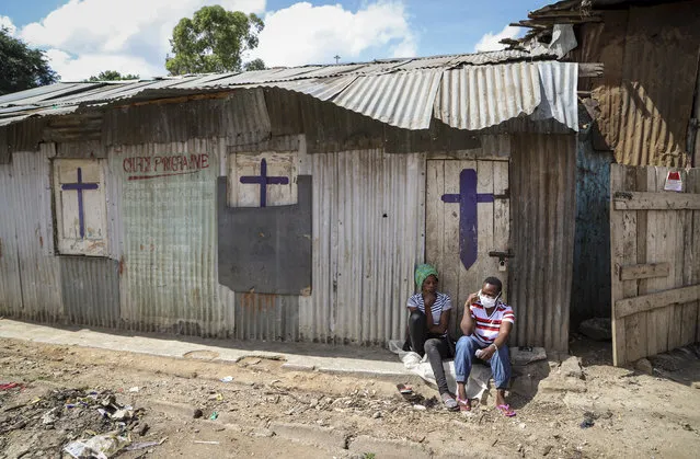 Two residents sit outside a closed church in the Mathare slum, or informal settlement, of Nairobi, Kenya, on Easter Sunday, April 12, 2020. Religious public services services have been stopped to limit the spread of coronavirus. (Photo by Patrick Ngugi/AP Photo)