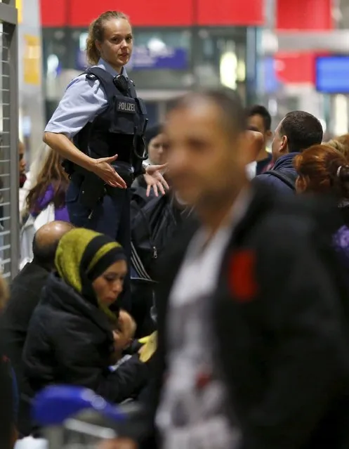 A German border policewoman stands on a bench while talking to migrants who unexpectedly disembarked a train that departed from Budapest's Keleti station, at the railway station of the airport in Frankfurt, Germany, early morning September 6, 2015. (Photo by Kai Pfaffenbach/Reuters)