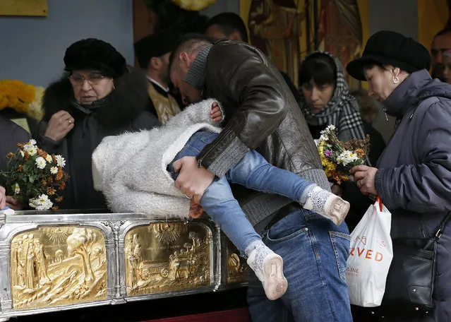 A Romanian father helps his boy to kiss the golden box containing the relics of Saint Dimitrie Basarabov during a mass attended by Kirill (not pictured), the Russian Orthodox Patriarch of Moscow and All Russia, at Patriarchal Cathedral in Bucharest, Romania, 27 October 2017. Russian Patriarch Kirill arrived yesterday at the invitation of his Romanian counterpart Daniel to take part at the pilgrimage at the relics of the Saint Dimitrie Basarabov, the patron saint of Romania's capital. The heads of Romanian and Russian Orthodox churches commemorate all the victims of the communist regimes in their countries who stand to defend their orthodox faith with the price of their liberty or life, during the morning mass. (Photo by Robert Ghement/EPA/EFE)