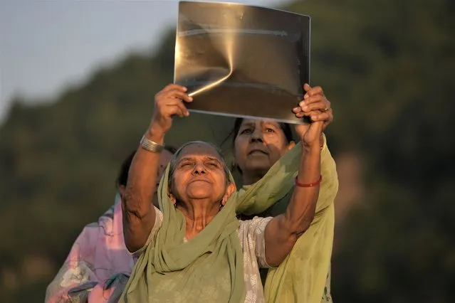 Women watch a partial solar eclipse through an X-ray film on the banks of Tawi River in Jammu, India, Tuesday, October 25, 2022. (Photo by Channi Anand/AP Photo)