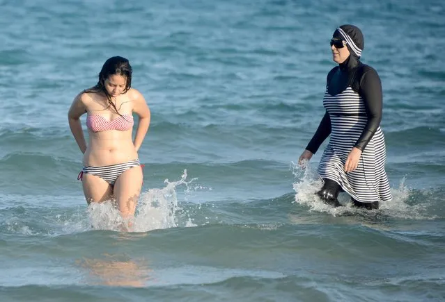 This file photo taken on August 16, 2016 shows Tunisian women, one (R) wearing a “burkini”, a full-body swimsuit designed for Muslim women, walking in the water at Ghar El Melh beach near Bizerte, north-east of the capital Tunis. The debate launched this summer in France over the Burkini is not causing such a stir in North Africa where the Islamic swimsuit is uncontroversial as the dress-code on the beaches has become increasingly prudish. (Photo by Fethi Belaid/AFP Photo)
