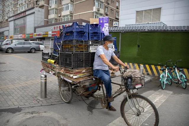 A man wearing a face mask to protect against the coronavirus pedals a cycle loaded with boxes and crates in Beijing, Saturday, July 11, 2020. (Photo by Mark Schiefelbein/AP Photo)