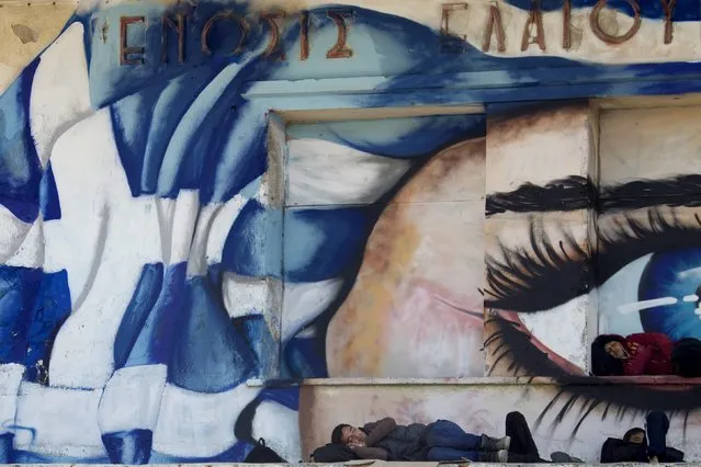 Refugees and migrants sleep in front of a graffiti covered wall  depicting a face and the Greek national flag at the port of the city of Mytilene on the island of Lesbos, Greece, October 6, 2015. Austrian Chancellor Werner Faymann is the first European Union leader on Tuesday to visit the Greek island of Lesbos to see the impact of Europe's migrant crisis on one of the refugees' preferred entry points into the EU. (Photo by Dimitris Michalakis/Reuters)