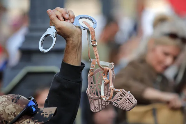 A man waves handcuffs attached to muzzles during a protest in Bucharest, Romania, Saturday, September 19, 2020. Several hundred Romanians, including many families with young children, held a protest in the country's capital against measures meant to curb the spread of the coronavirus, especially social distancing and the mandatory use of masks in schools. (Photo by Vadim Ghirda/AP Photo)