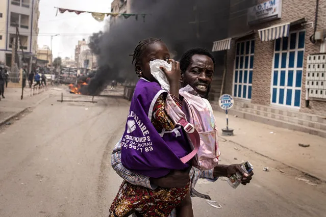 A man runs with his daughter as she covers her nose from teargas in Dakar on March 16, 2023. Security forces were deployed in the Senegalese capital Dakar on March 16, 2023 ahead of a politically-charged trial of an opposition leader. Ousmane Sonko is being tried for allegedly defaming a minister, a case that could determine whether he will be eligible to run in presidential elections next February. (Photo by John Wessels/AFP Photo)