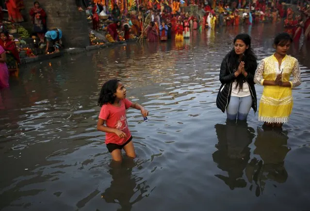 A girl holding her watch walks in the Bagmati river as devotees offer prayers to the setting sun during the "Chhat" festival in Kathmandu, Nepal November 17, 2015. (Photo by Navesh Chitrakar/Reuters)