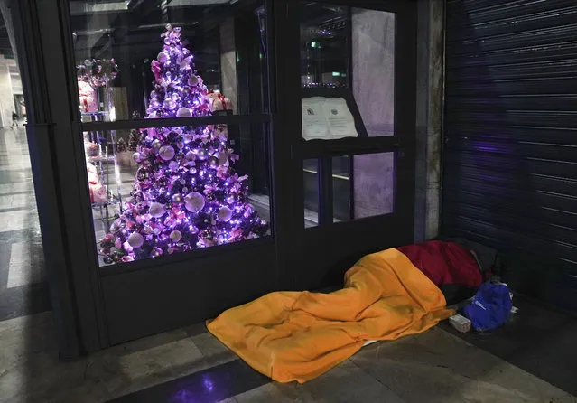 A homeless sleeps on the floor next to Christmas decoration outside a restaurant in downtown Milan, northern Italy, Friday, November 27, 2020. Nowhere in Italy is poverty more evident than in Lombardy, the northern region that has been the pandemic epicenter in both surges. The Coldiretti agriculture lobby estimates that the virus has created 300,000 so-called “new poor”,' based on surveys of the dozens of charity associations operating in the region. (Photo by Luca Bruno/AP Photo)