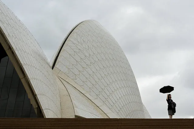 A woman holds up an umbrella at the Sydney Opera House during cloudy and rainy weather conditions in Sydney, Australia on April 20, 2023. (Photo by Jaimi Joy/Reuters)