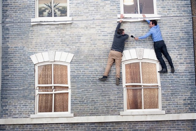 People appear dangling as a large-scale installation art piece by Leandro Erlich, named “Dalston House”, is displayed on June 24, 2013 in London, England. Part of the “Beyond Barbican” summer series of events, the interactive installation is a full facade of a late nineteenth-century Victorian terraced house built on the ground with a large mirror above it to reflect people as to appear dangling from the structure.  (Photo by Dan Dennison/Getty Images)