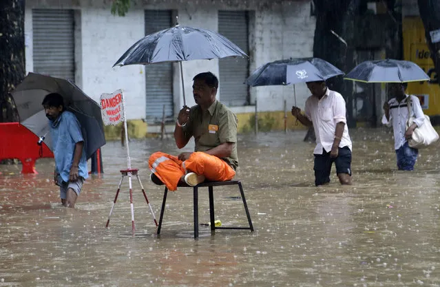 A local municipal worker sits on guard near an open manhole on a waterlogged street in Mumbai, India, Tuesday, July 3, 2018. Heavy rainfall has disrupted normal life in the commercial capital with many areas left waterlogged. (Photo by Rajanish Kakade/AP Photo)