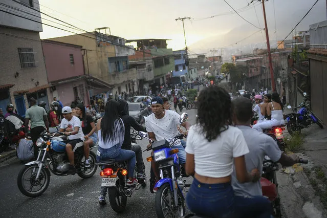 Motorcycle riders gather to see stuntman Pedro Aldana do an exhibition performance in Caracas, Venezuela, Sunday, January 31, 2021. The 33-year-old makes a living with his shows inspiring his young fans who flock to his shop, where he teaches them to change the oil and tune up their bicycles. (Photo by Matias Delacroix/AP Photo)