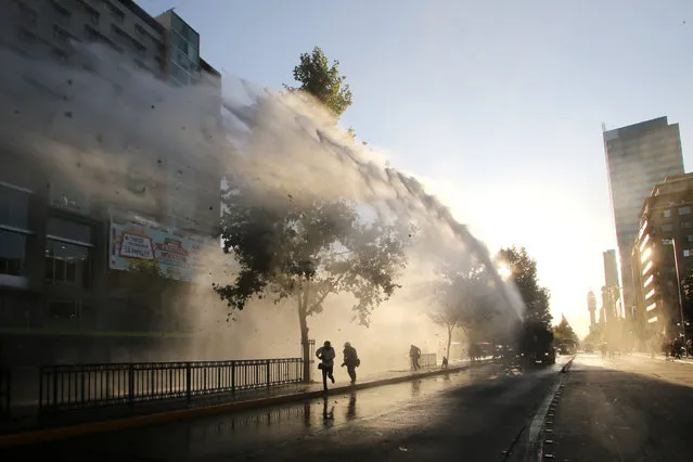 Riot police throw water at students during a demo in demand of free state universities and for the quality of public education in Santiago, on December 22, 2015. (Photo by Claudio Reyes/AFP Photo)