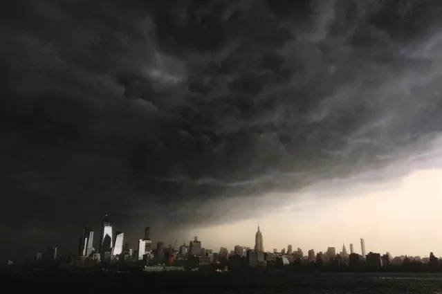 In this Tuesday, May 15, 2018 photo, storm clouds gather over New York city seen from the Hudson River. A line of strong storms pushed across New York City and badly disrupted the evening commute, stranding thousands of train riders. (Photo by Denis Paquin/AP Photo)
