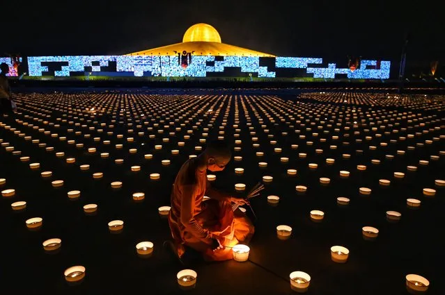 A Buddhist monk lights candles to commemorate Visakha Bucha Day or Vesak Day, a celebration of the birth, enlightenment and death of the Lord Buddha held on the full moon of the third lunar month in the Buddhist calendar, at Wat Dhammakaya Buddhist temple on the outskirts of Bangkok on May 26, 2021. (Photo by Lillian Suwanrumpha/AFP Photo)