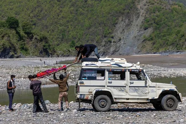 Relatives of Pramila Devi, 36, who died from complications related to the coronavirus disease (COVID-19), take down her body from a jeep before her cremation, on the banks of the river Ganges in Pauri Garhwal, in the northern state of Uttarakhand, India, May 24, 2021. Devi's eldest daughter got married and moved away in late April after the family hosted a ceremony attended by over two dozen people, her husband Suresh Kumar, 43, told Reuters. Two weeks after that Devi suffered a bout of diarrhoea. But it was not until 10 days later that Kumar, who has no income and depends on handouts, took her to a nearby dispensary that has been turned into a small COVID-19 facility with four beds. Devi tested positive for COVID-19 with very low blood oxygen levels. She died a day later. (Photo by Danish Siddiqui/Reuters)